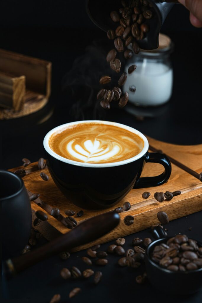 Latte art in a black cup surrounded by roasted coffee beans.